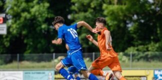 man in blue and orange jersey shirt running on green grass field during daytime