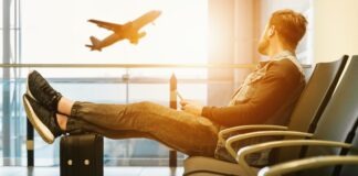 man sitting on gang chair with feet on luggage looking at airplane