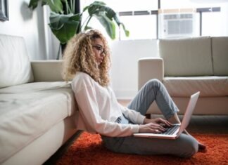 What to Look For Before Buying From a Furniture Shop USA woman sitting on floor and leaning on couch using laptop