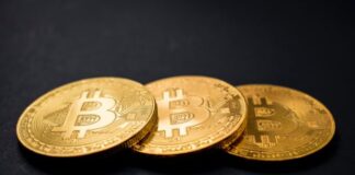 three gold-colored bitcoins on black surface