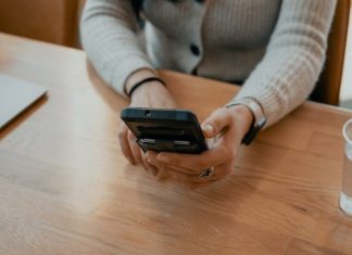woman in white sweater holding black smartphone