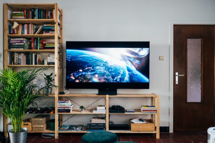 Photo by Jonas Leupe black flat screen tv turned on near brown wooden shelf