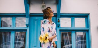woman in white and blue floral dress holding yellow flower bouquet standing beside blue wooden window