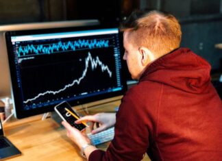 Key Differences Between the Stock Market and the Bitcoin Market! man holding black smartphone with flat screen monitor in front
