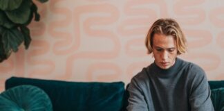 man in gray turtle neck shirt sitting on blue couch using a Microsoft Surface 3 sandstone laptop