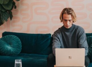 Top 5 AI Image Enlarger with Quick Guide man in gray turtle neck shirt sitting on blue couch using a Microsoft Surface 3 sandstone laptop
