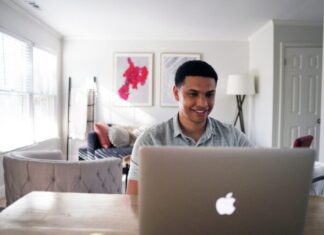 man in gray hoodie sitting on chair in front of silver macbook