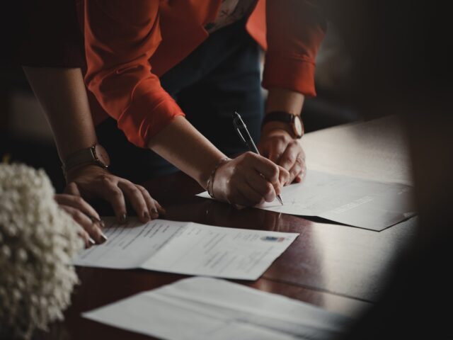Photo by Romain Dancre person in orange long sleeve shirt writing on white paper