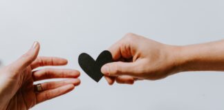 person reaching black heart cutout paper