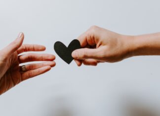 person reaching black heart cutout paper