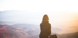 person sitting on top of gray rock overlooking mountain during daytime
