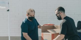 man in blue crew neck t-shirt standing beside brown cardboard boxes