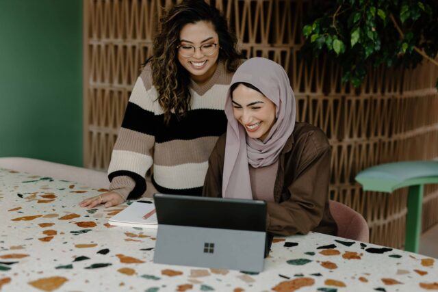 Photo by Microsoft 365 Two women sitting at a table with a laptop