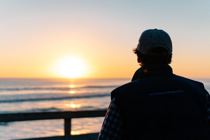 Photo by Douglas Bagg a man looking out at the ocean at sunset