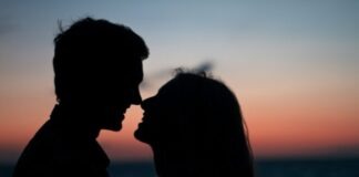 silhouette of man and woman about to kiss on beach during sunset