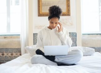 A person sitting on a bed using a computer Description automatically generated