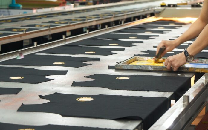 Photo by Đồng Phục Hải Triều a person cutting fabric on a conveyor belt
