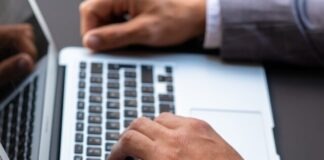 person wearing black leather strap gold round analog watch using macbook pro