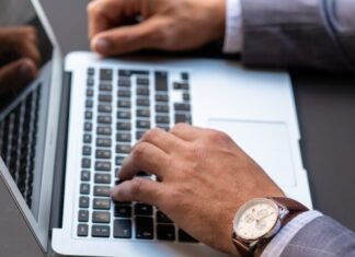 person wearing black leather strap gold round analog watch using macbook pro