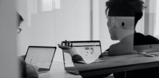 Two people at a table with laptops discussing how to write a request for proposal.