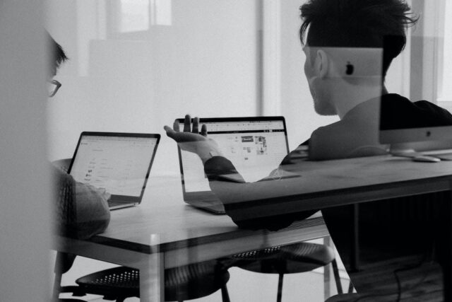 img Two people at a table with laptops discussing how to write a request for proposal.