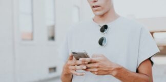 man in white crew-neck top using smartphone outdoors