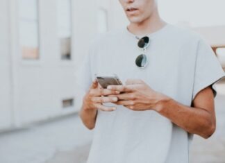 man in white crew-neck top using smartphone outdoors