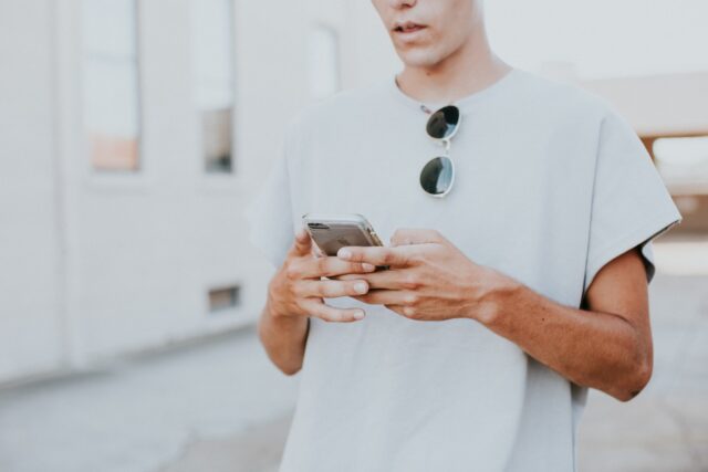 Photo by Hannah Busing man in white crew-neck top using smartphone outdoors