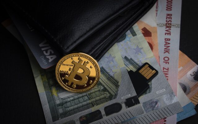 Photo by Aleksi Räisä a bitcoin sitting on top of a pile of money