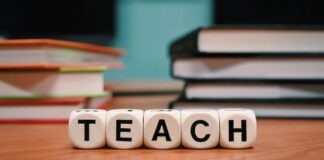 A stack of books and dice spelling the word teach Description automatically generated