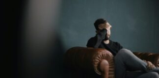 a man holds his head while sitting on a sofa