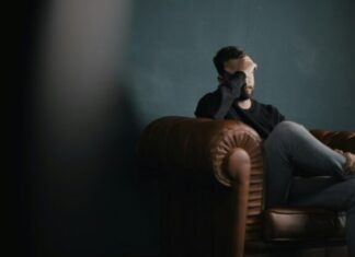 How to Tame Chronic Stress Gone Wild a man holds his head while sitting on a sofa