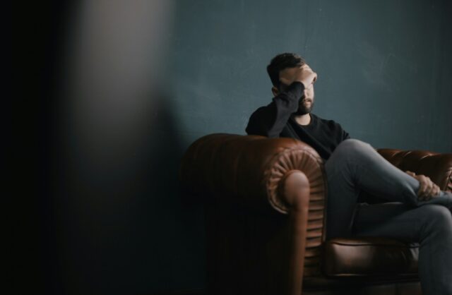 Photo by Nik Shuliahin ðð a man holds his head while sitting on a sofa