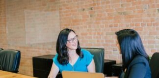 woman in teal t-shirt sitting beside woman in suit jacket
