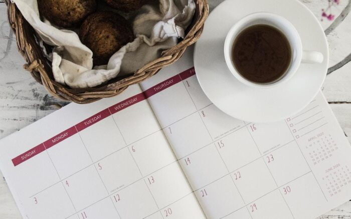A journal with a coffee cup on top of it and bread in the background.