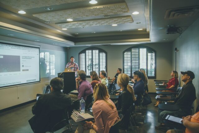Photo by Kenny Eliason a group of people in a room with a projector screen