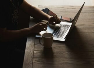 gray laptop computer on brown wooden table beside person sitting on chair