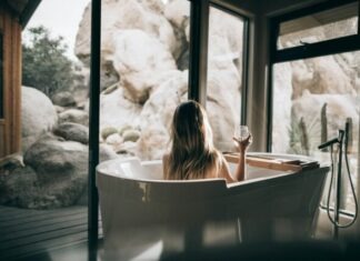 8 Self-Care Items Everyone Needs woman in white bathtub holding clear drinking glass