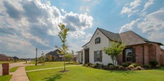 white and brown house near green grass field under white clouds and blue sky during daytime