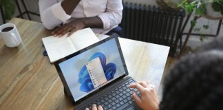 Overhead view of two people at a table working with a Microsoft laptop and notebook