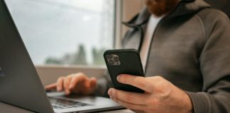 a man sitting in front of a laptop computer holding a cell phone