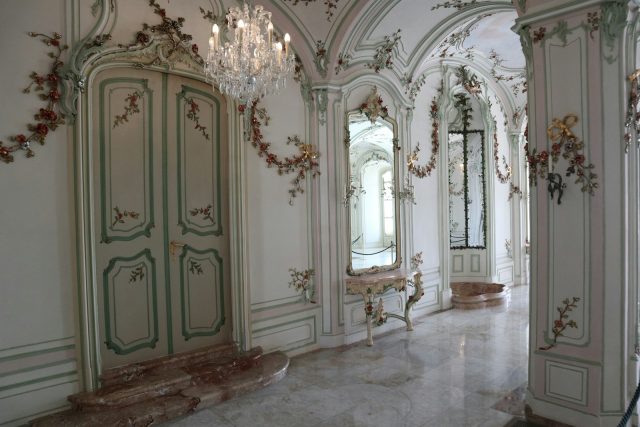 Photo by Balint Miko A hallway with a chandelier and a marble floor