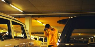 man holding cap standing between car on parking lot