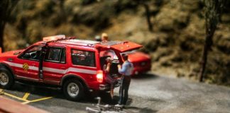 a miniature scene of a red car with a man standing next to it