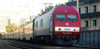 a red train traveling down train tracks next to a tall building