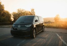 Evolving Travel Demands Influencing Motor Coach Rental Industry Innovation Trends A black van driving down a road next to a forest