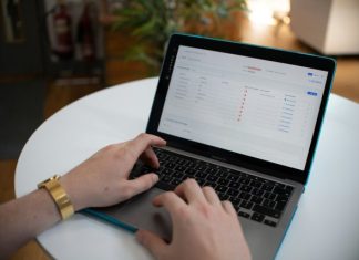 Hands typing on a laptop with a spreadsheet on screen.