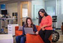 The Importance of Knowledge Management in Corporate Environments Two women on an orange couch, focused on their laptops, discussing Knowledge Management in a corporate environment.