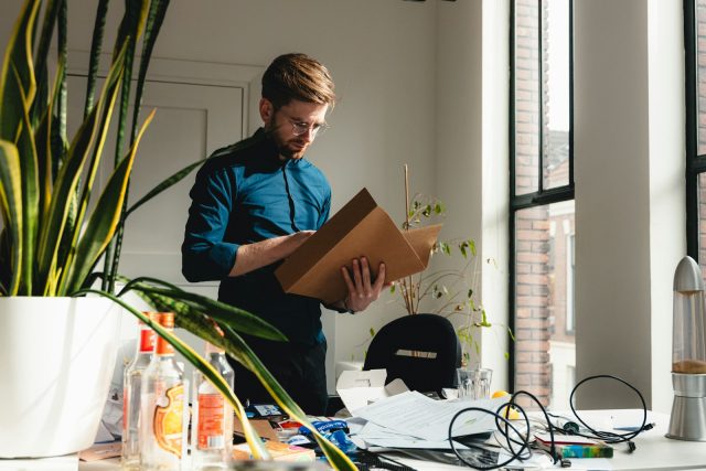 Photo by Tim van der Kuip a man standing in an office holding a box