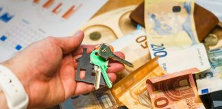 Hand holding house keys over euro banknotes and charts.